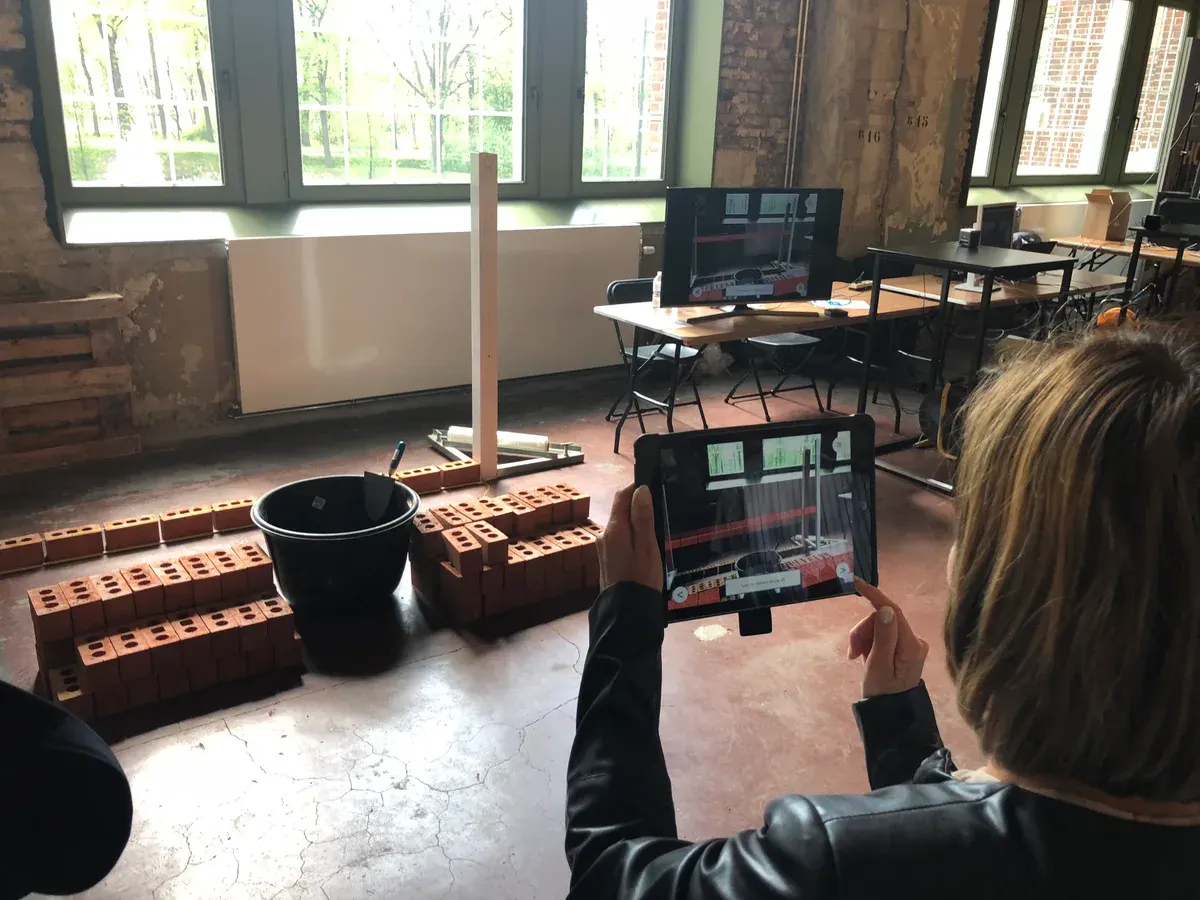 A learner holding a tablet in front of a practice wall in a masonry training centre.